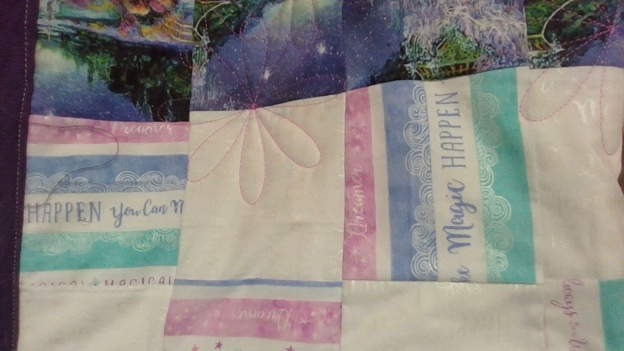 Colorful quilt with text patterns, including phrases like 'Magic Happens' in pastel shades.